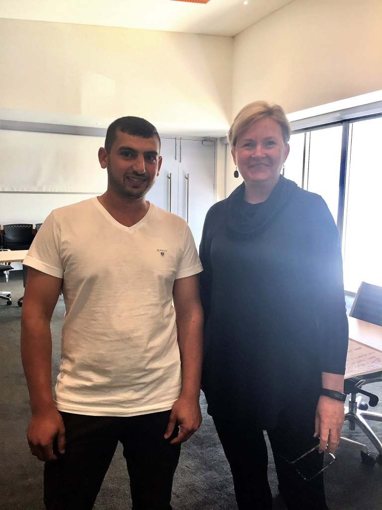 Hussam Saraf standing with a community contact indoors during the Ask the Cows project journey.