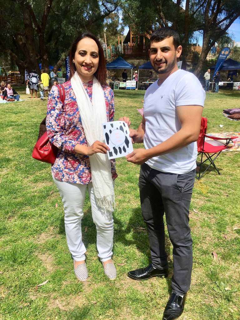 Hussam Saraf and a community member holding Ask the Cows at an outdoor gathering.