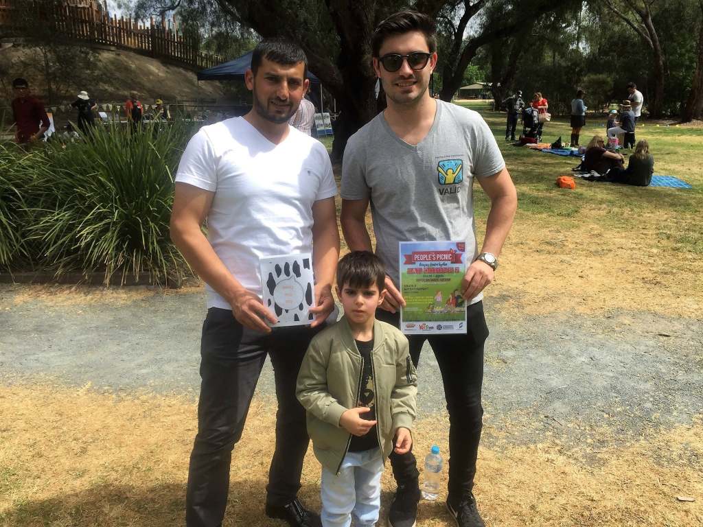 Hussam Saraf with an adult and child, holding books at an outdoor community event.