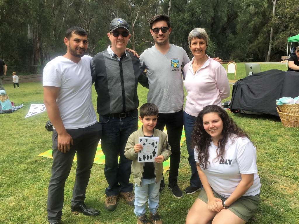 Hussam Saraf with a group of adults and a child holding Ask the Cows at an outdoor community gathering.