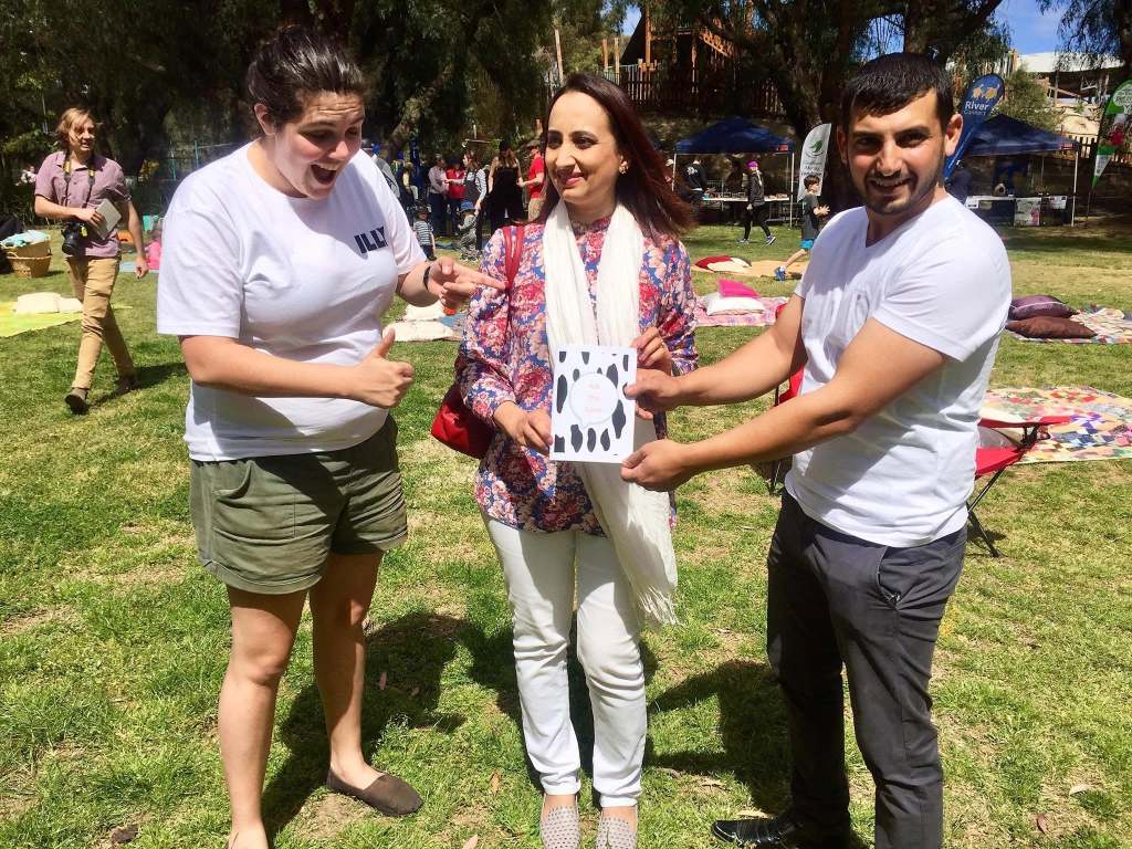 Hussam Saraf and two community members looking at Ask the Cows at an outdoor event.