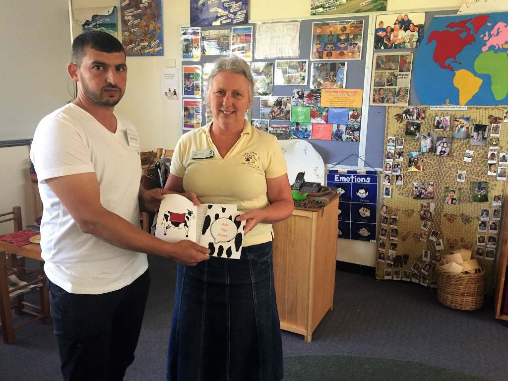 Hussam Saraf and a staff member holding Ask the Cows beside community displays and a world map.