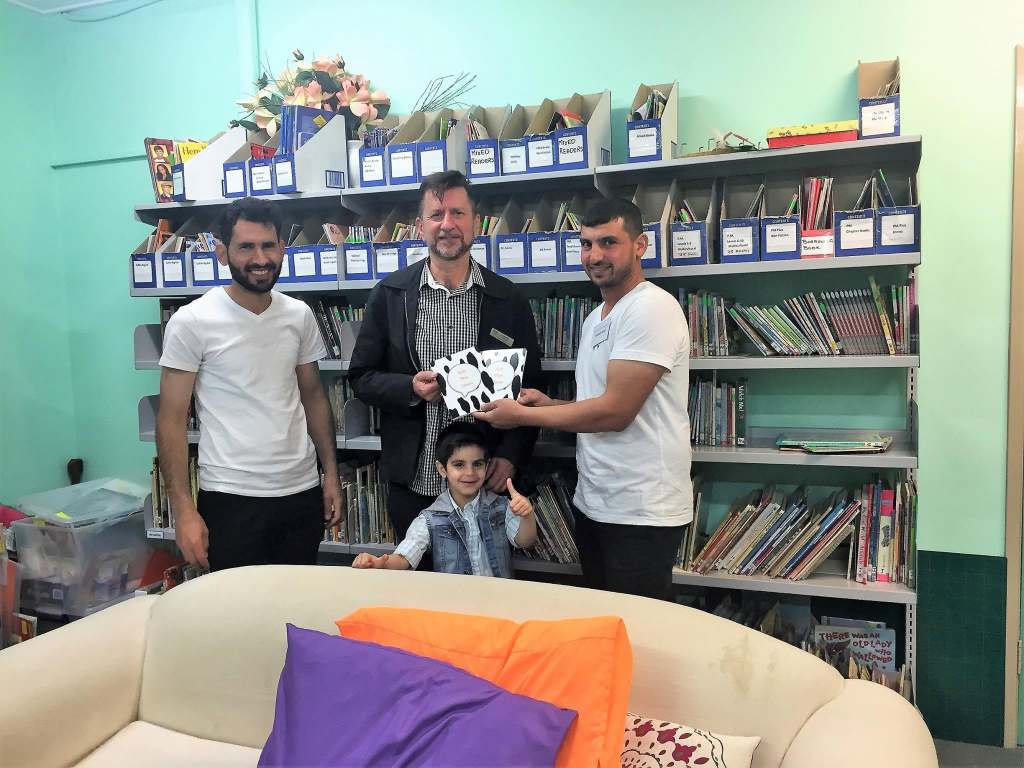 Hussam Saraf with two adults and a child beside a bookcase, sharing Ask the Cows.