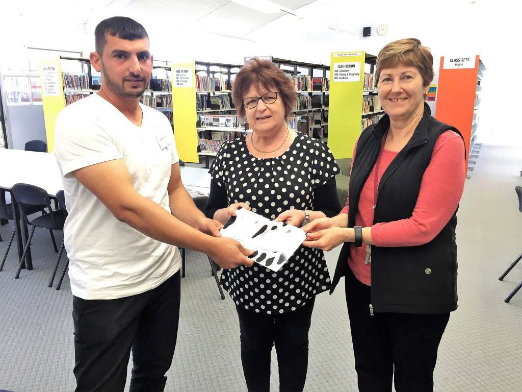 Hussam Saraf with two library staff members holding copies of Ask the Cows.