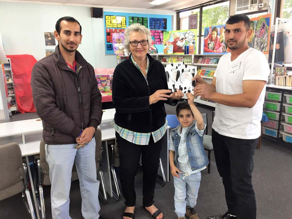 Hussam Saraf with two adults and a child, presenting Ask the Cows in a library setting.