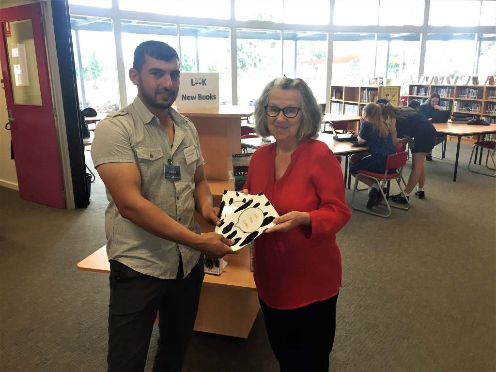 Hussam Saraf and a staff member holding copies of Ask the Cows at a library.