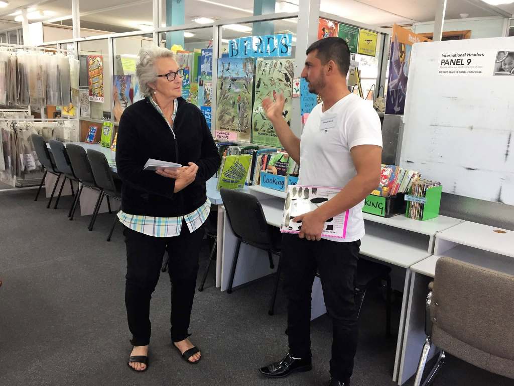 Hussam Saraf discussing Ask the Cows with a staff member while holding copies in a library setting.