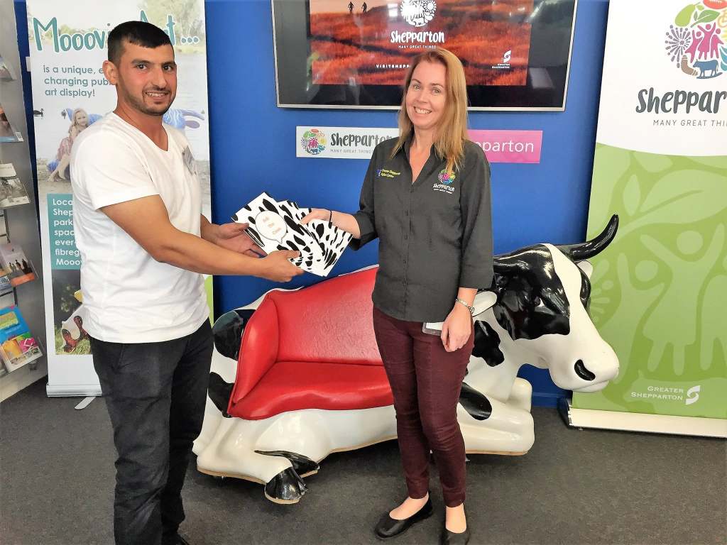 Hussam Saraf and a staff member holding Ask the Cows beside a cow sculpture and a Visit Shepparton display.
