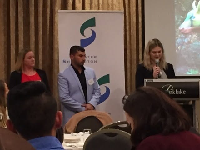 Hussam Saraf standing with fellow presenters while one speaks into a microphone at the Parklake lectern.