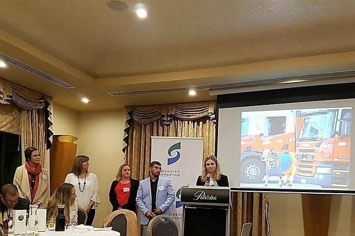 A group presenting beside a Greater Shepparton banner and a projected photograph of a cow sculpture and fire engines.
