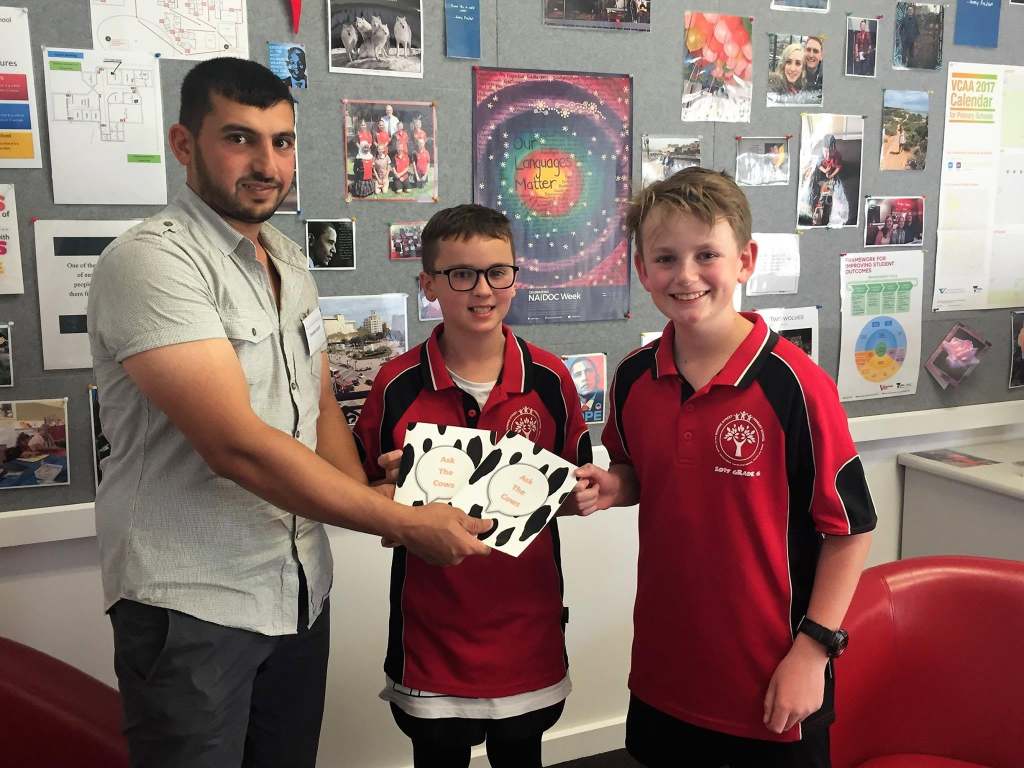 Hussam Saraf sharing Ask the Cows with two students in red school uniforms.
