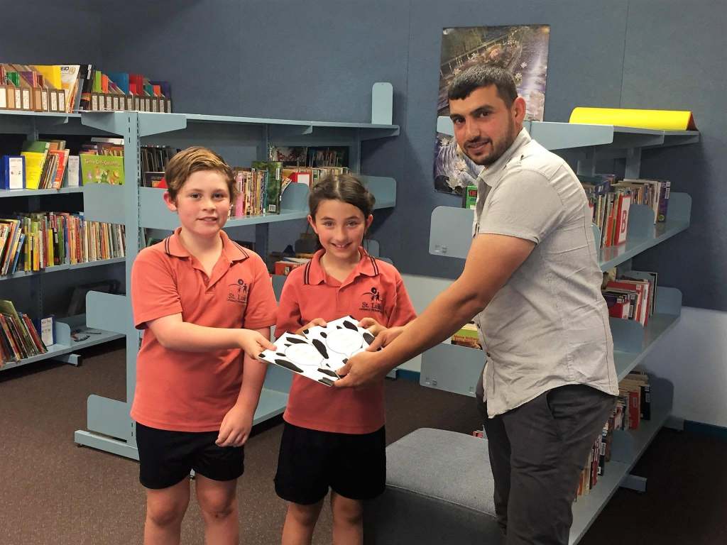 Hussam Saraf presenting Ask the Cows to two students in a school library.