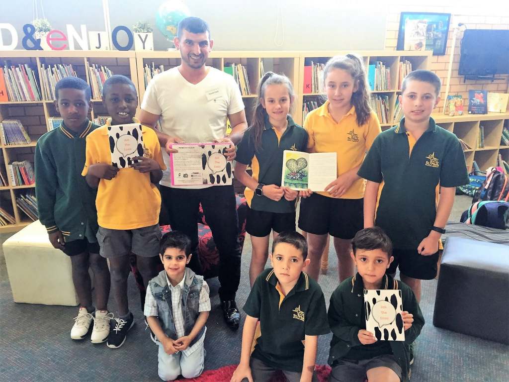 Hussam Saraf with a group of children holding books in a school library.