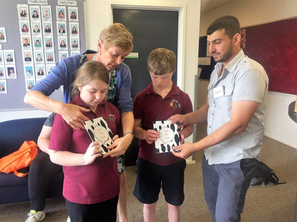 Hussam Saraf and an adult helping two students look through copies of Ask the Cows.