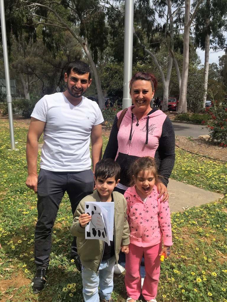 Hussam Saraf with an adult and two children outdoors, with a child holding an Ask the Cows storybook.