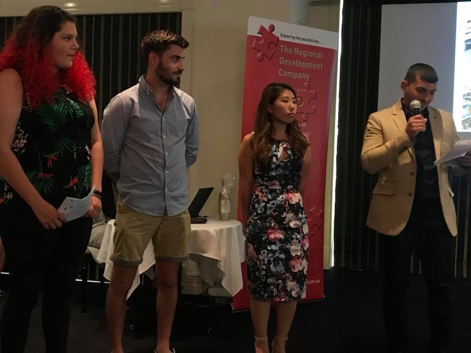 Hussam Saraf speaking into a microphone alongside fellow participants at the Community Leadership Program graduation.