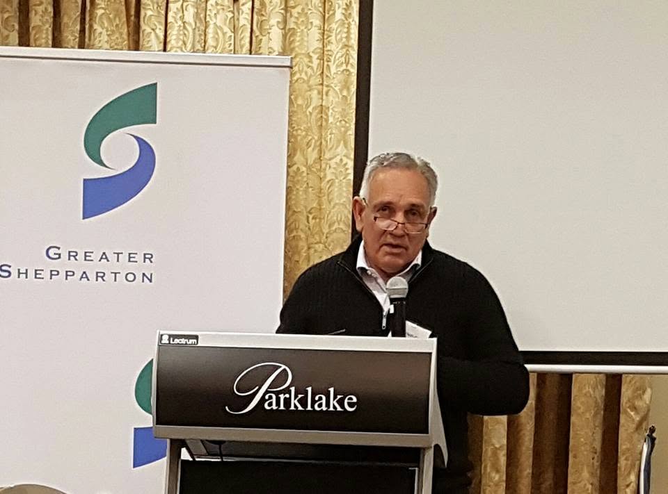 A speaker holding a microphone behind the Parklake lectern beside a Greater Shepparton banner at the networking dinner.