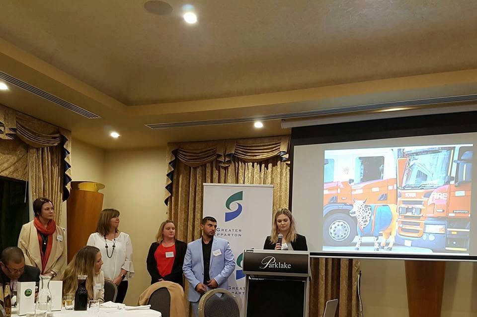 Hussam Saraf and fellow participants presenting beside a Greater Shepparton banner and a projected Moooving Art cow at the networking dinner.