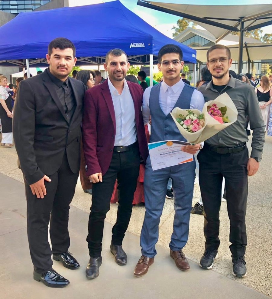 Four people posing beside a blue canopy, with a graduate holding flowers. GSSC Class of 2025.
