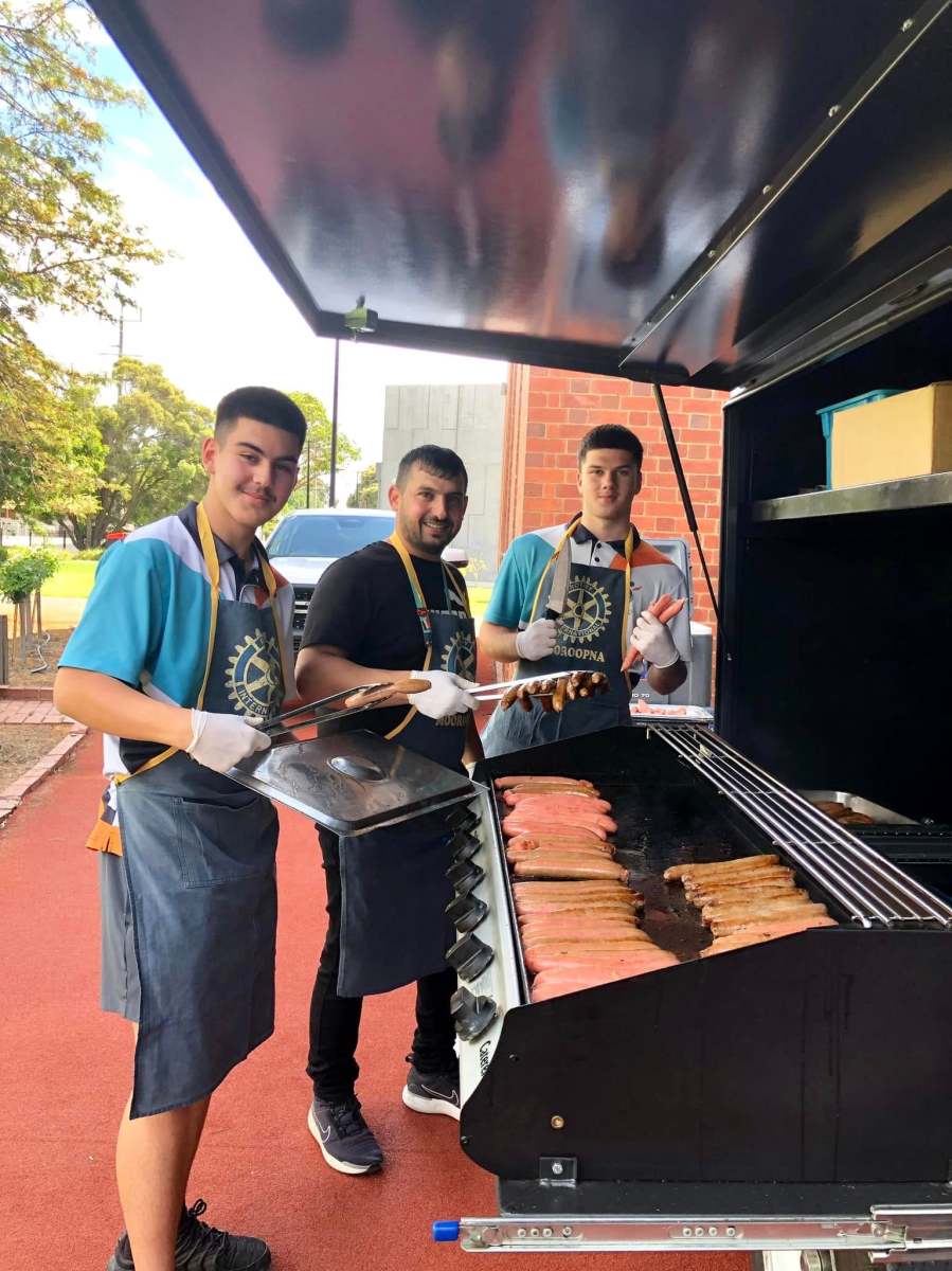 Three volunteers wearing Rotary Mooroopna aprons and preparing food at the barbecue.