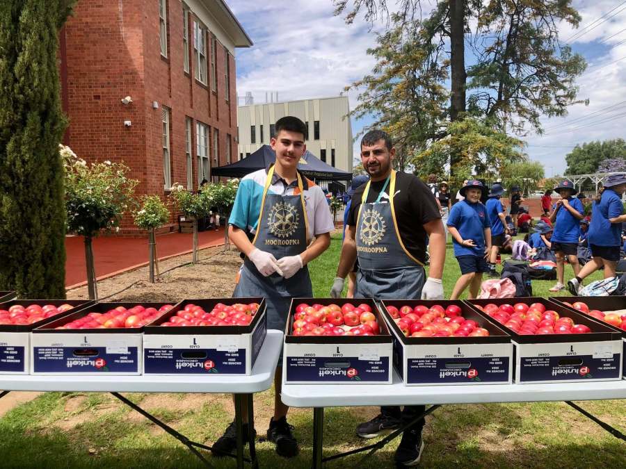 Two volunteers in Rotary Mooroopna aprons standing behind boxes of apples at GSSC.