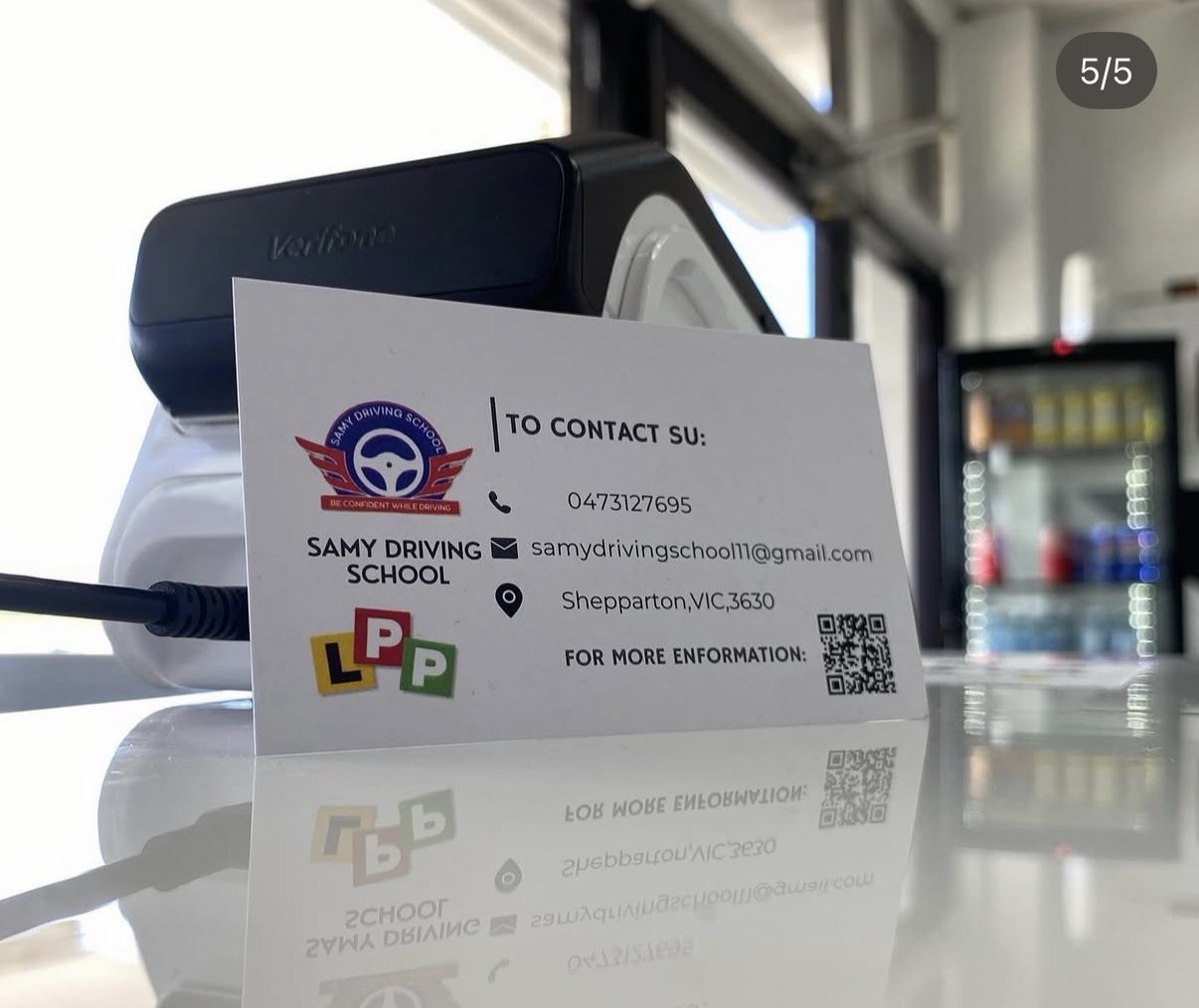 Printed Samy Driving School business card designed by Hammood AL-Badry, displayed beside a payment terminal.