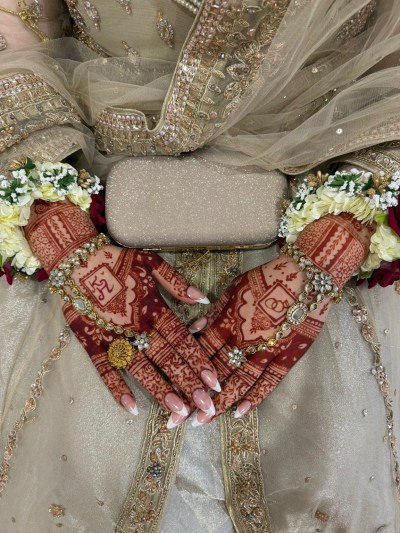 Henna by Diya: intricate patterns across both hands and wrists, with jewellery and a gold clutch.