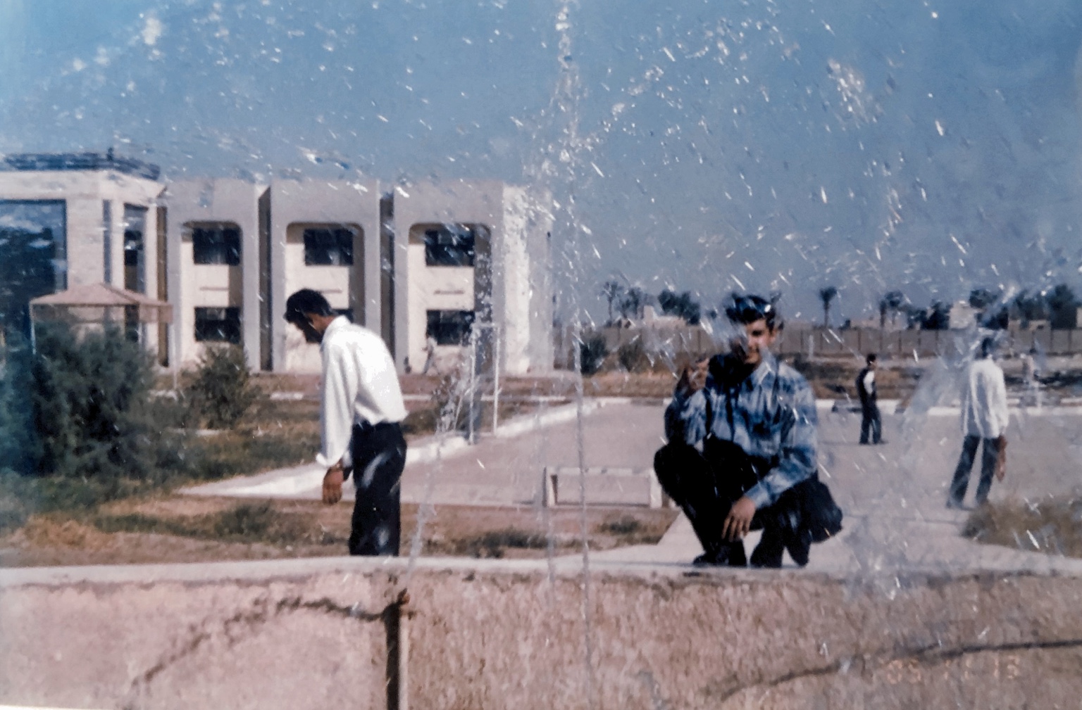 حسام الصراف قرب نافورة المعهد التقني في الديوانية أثناء الدراسة، وتظهر مباني المعهد في الخلفية.