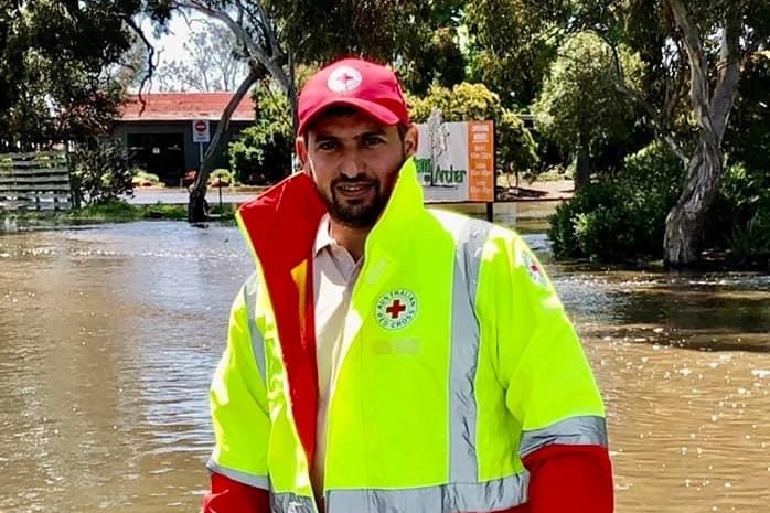Hussam Saraf wearing a Red Cross cap and high-visibility vest beside floodwater.