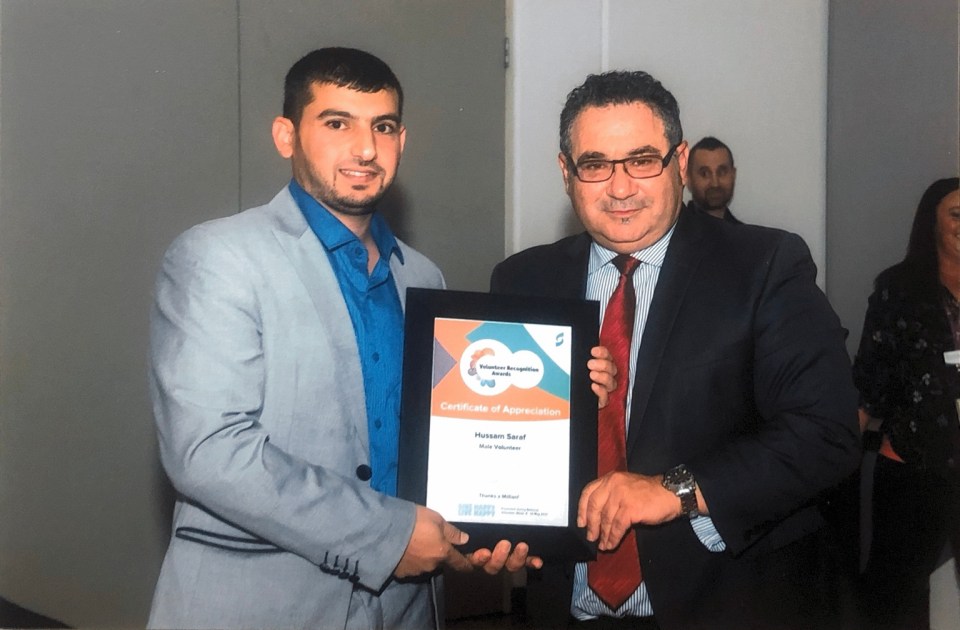 Hussam Saraf and another attendee holding his framed Male Volunteer Certificate of Appreciation in 2017.