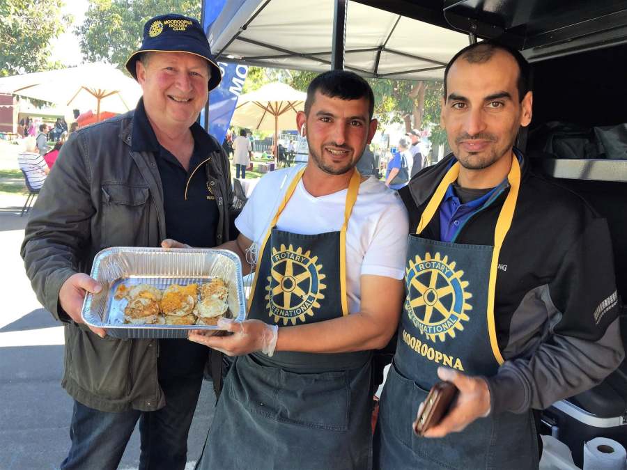 Three Rotary volunteers holding a tray of cooked food beside the catering trailer.