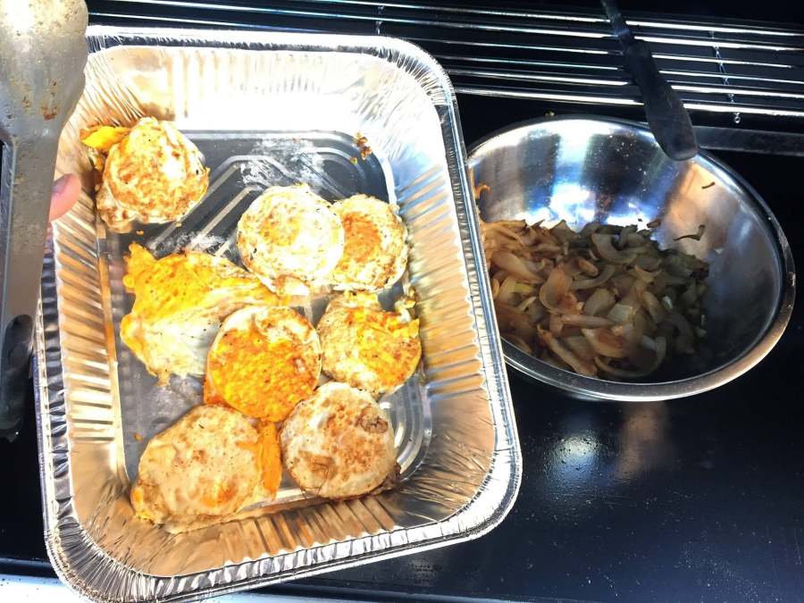 A tray of cooked eggs and a bowl of onions beside the barbecue.