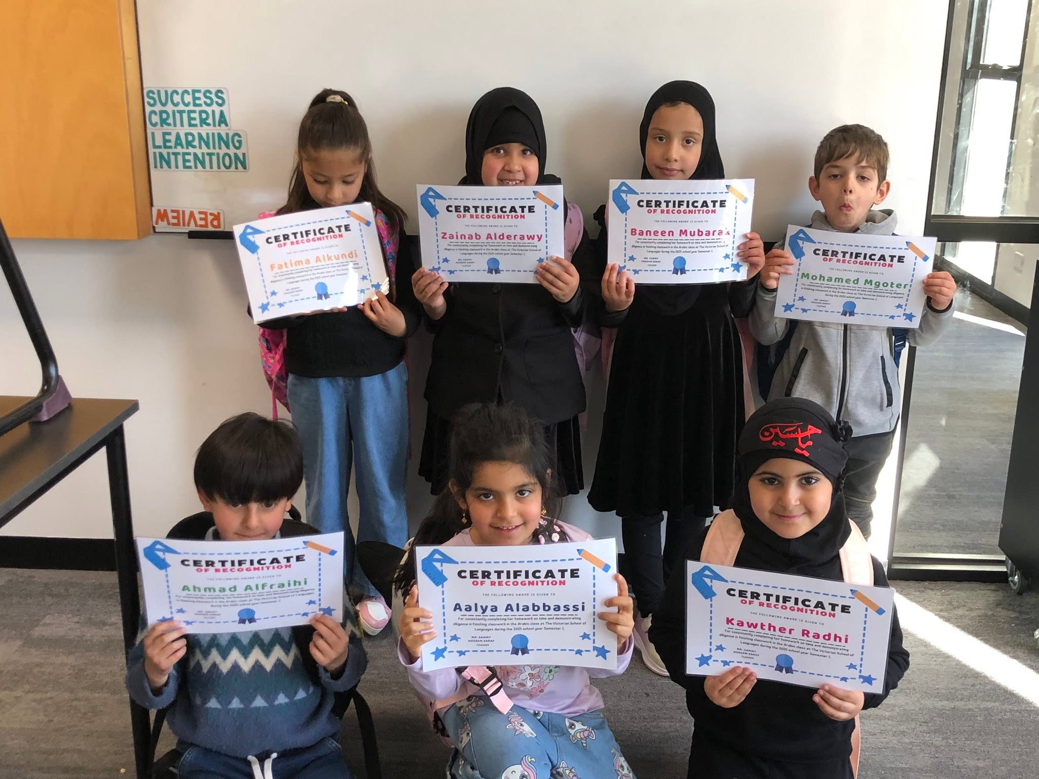 Young learners displaying their classroom achievement certificates.