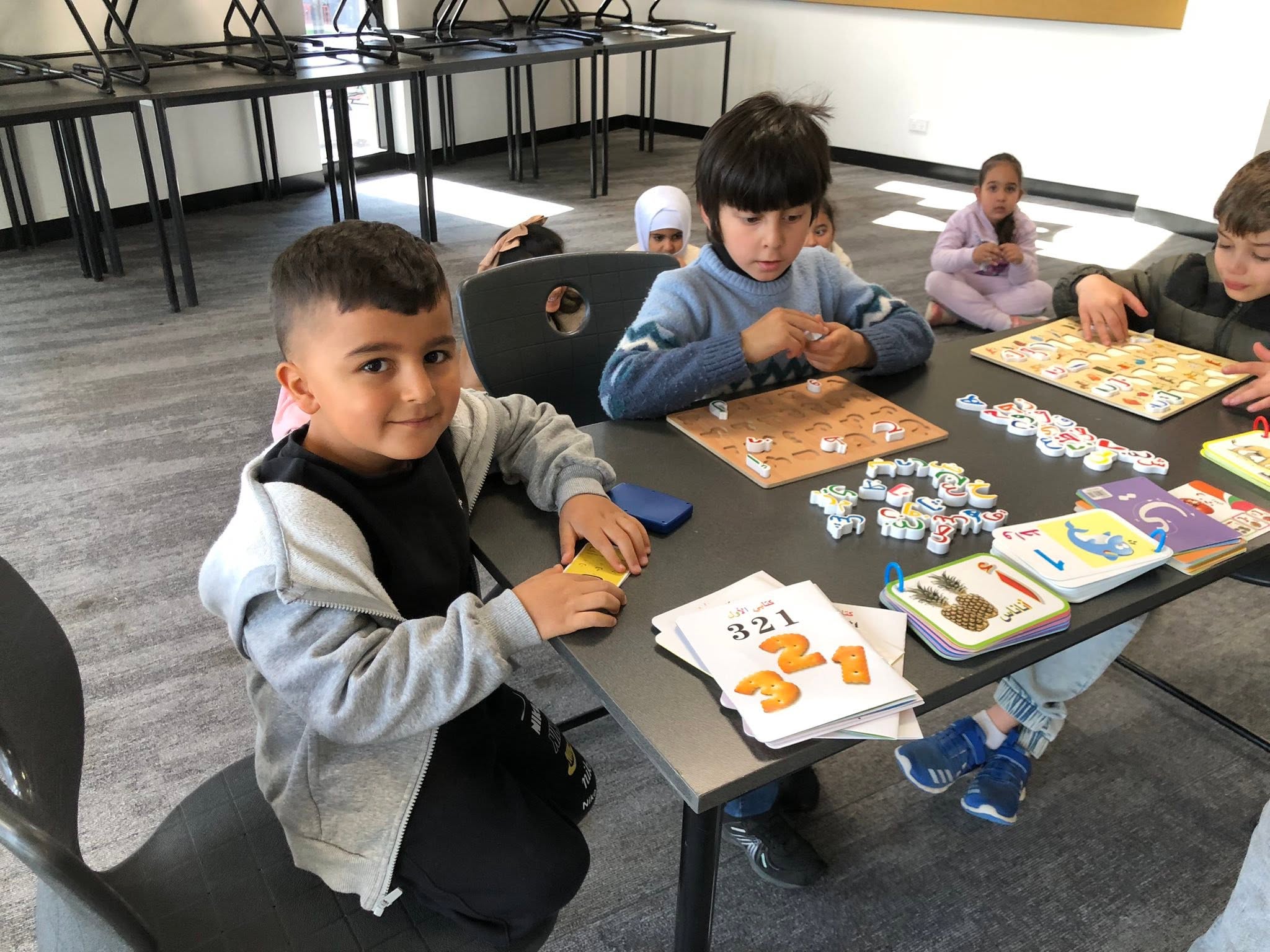 Young learners exploring illustrated books, puzzles and matching activities at a classroom table.