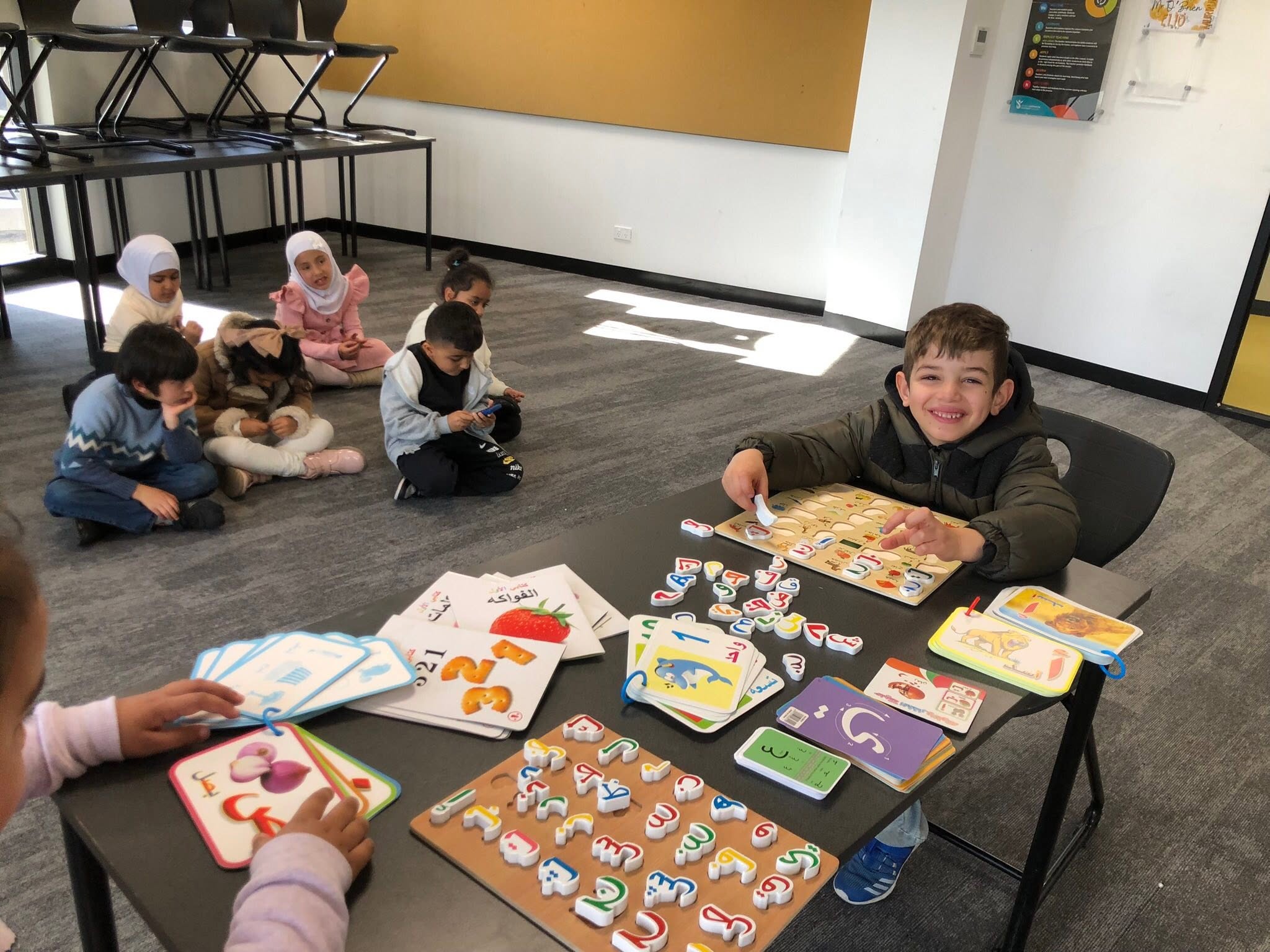 Young learners using illustrated books and puzzles, with another group working together on the classroom floor.