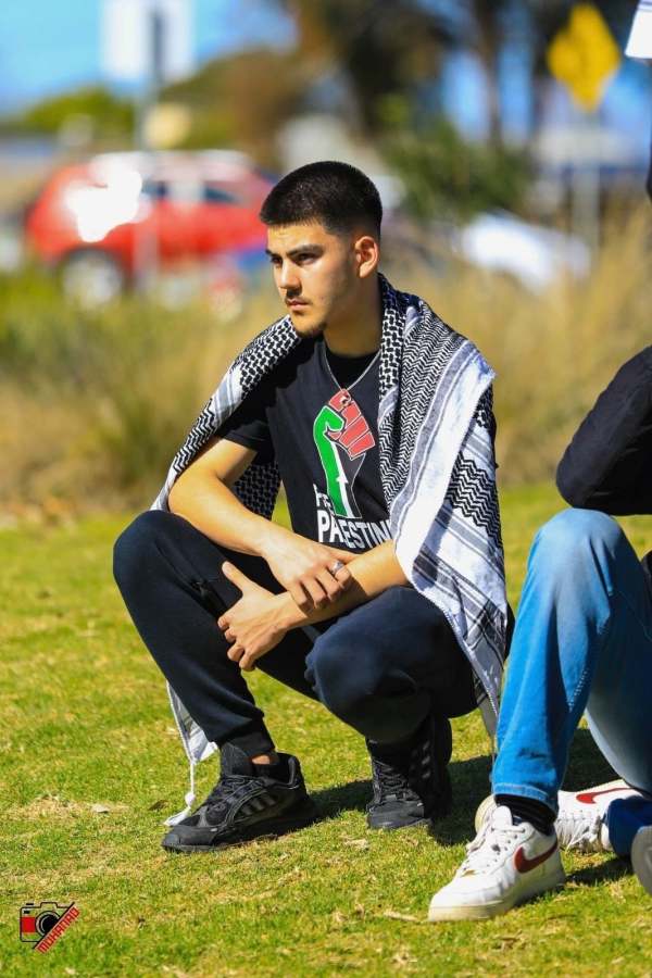 Kadir Sut seated outdoors, wearing a black shirt and patterned scarf.
