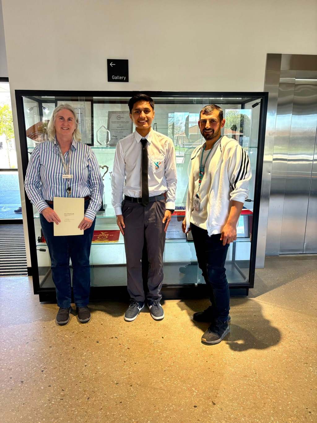 Charlotte Drinnan, Safa Zahir and Hussam Saraf standing together beside GSSC’s awards display.