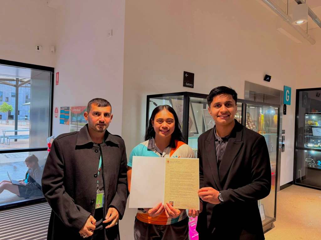 Three people posing indoors with an open presentation folder.