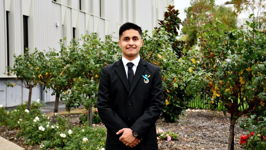 Safa Zahir standing outdoors in a black suit and tie for a Youth Parliament news portrait.