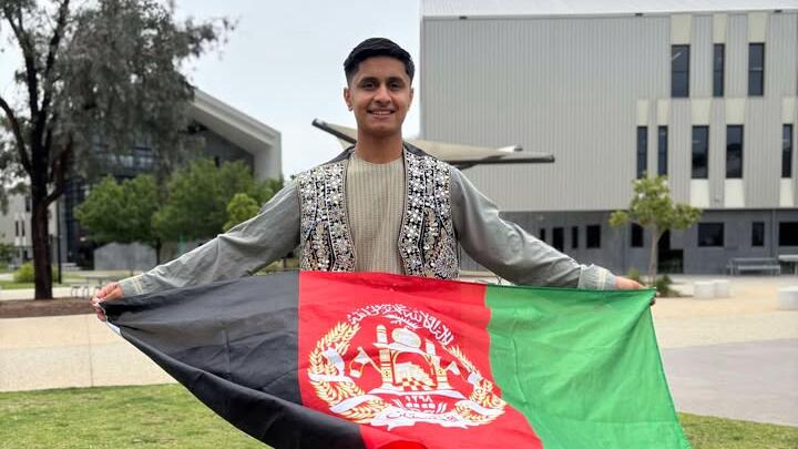 Safa Zahir standing outdoors in traditional clothing while holding an Afghan flag.