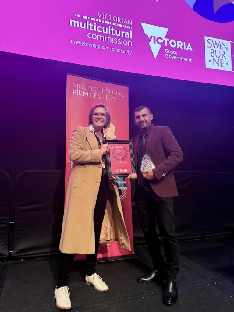 Two festival attendees displaying The Way to Freedom’s framed Official Selection certificate and winner trophy.
