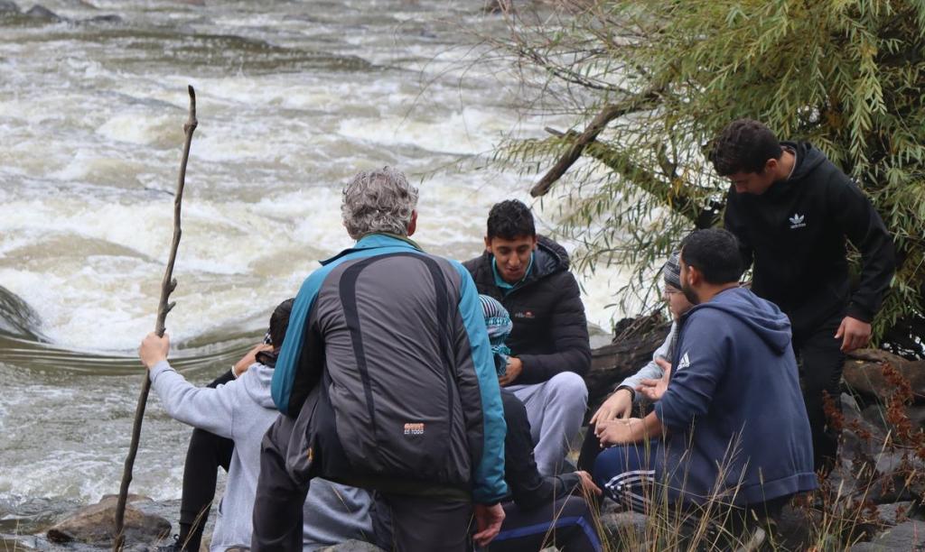 Film participants and a crew member gathered beside a river during production.
