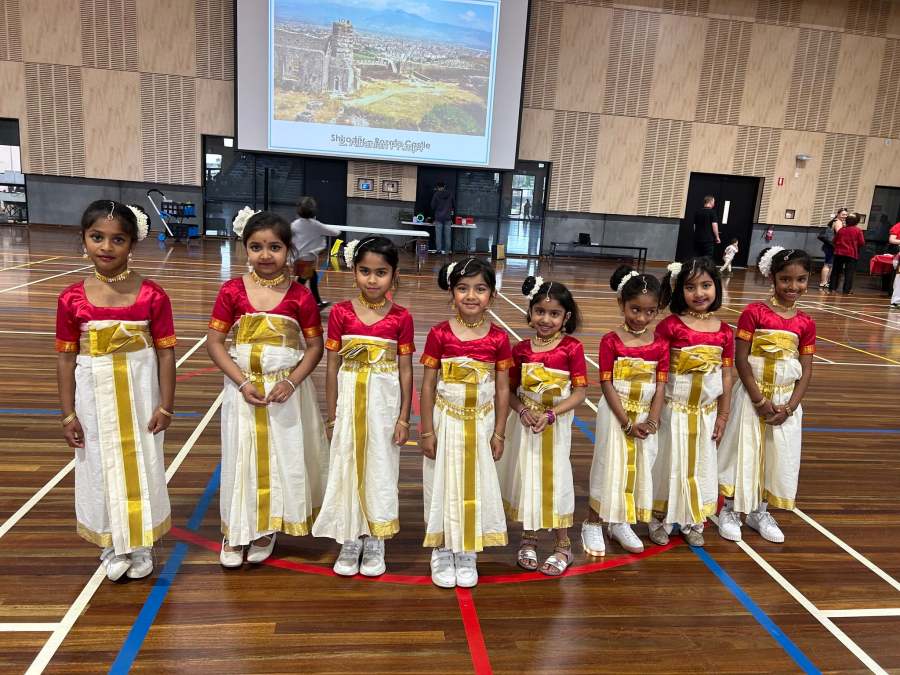Young performers in red, white and gold costumes posing together in the Expo hall.