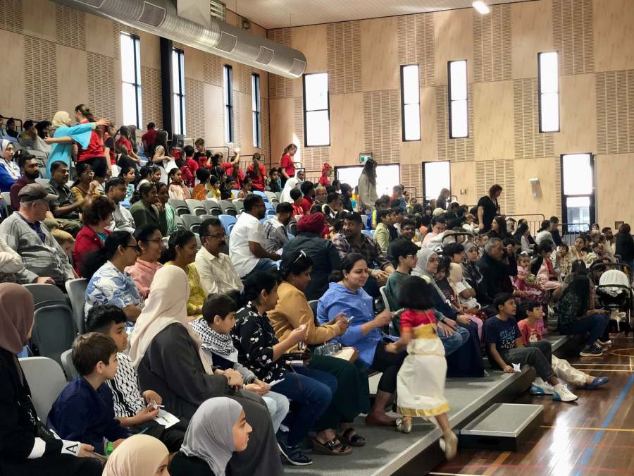 A seated audience of students, families and community members in the hall.